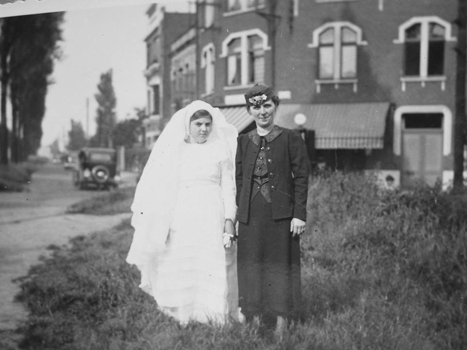 Photo ancienne en noir et blanc : une jeune fille en robe blanche et une femme posent devant la maison du Triez à Mouvaux