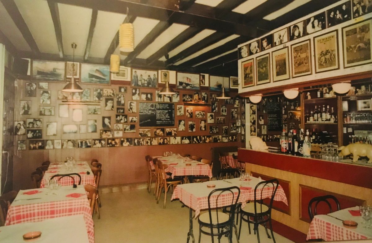 Ancienne salle du restaurant Le Triez, avec nappes à carreaux rouges, poutres sombres, comptoir rouge et murs couverts de photos encadrées
