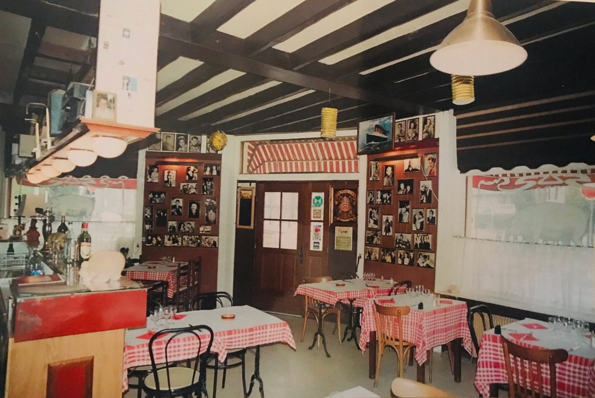 Ancienne salle du Triez avec tables à nappes à carreaux, porte en bois et portraits en noir et blanc aux murs
