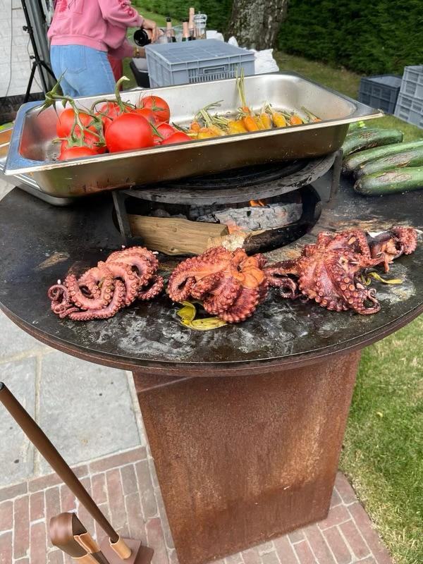 Poulpes grillés sur une plancha en acier, tomates en arrière-plan